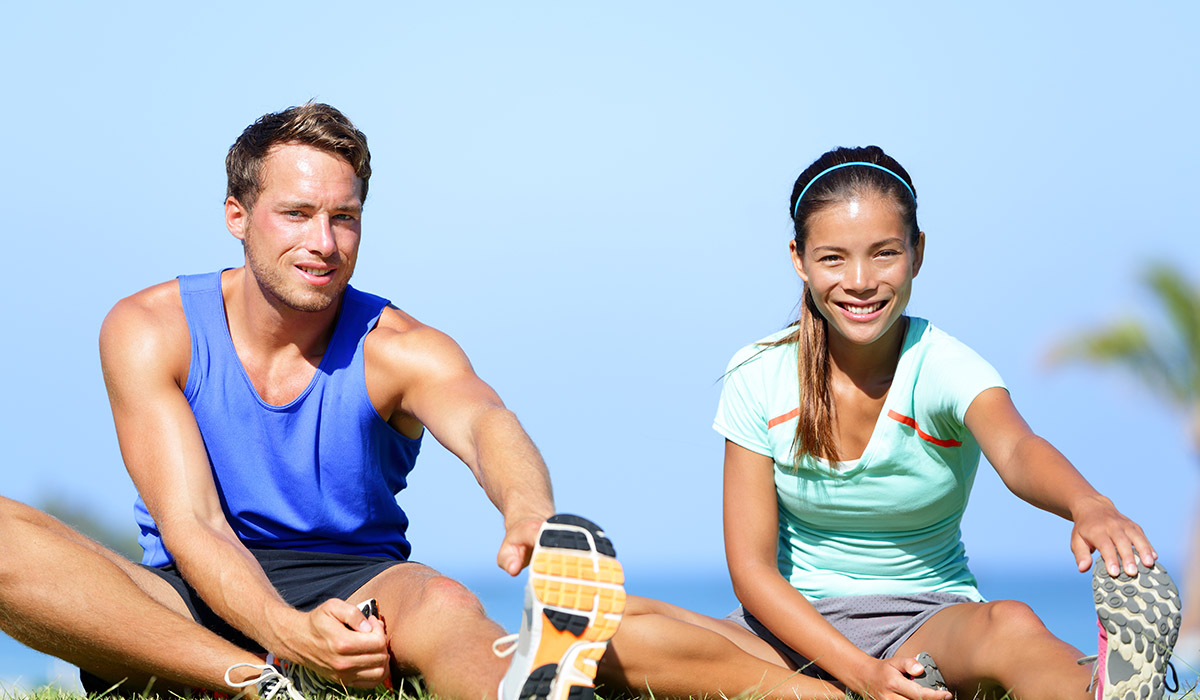 Stretching exercises - Fitness couple outside doing stretches exercise. Fit woman and man doing hamstring leg stretching training in summer. Beautiful multiracial couple.